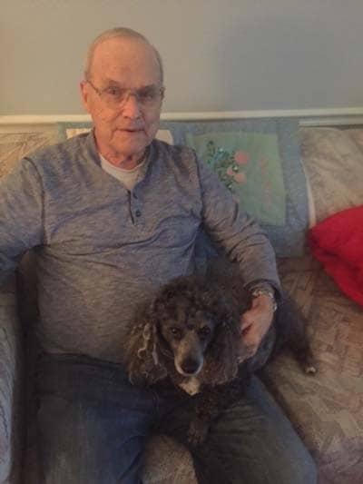 Paul with his arm around his dog Tuxedo, sitting on the couch.