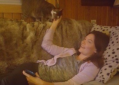 woman and cat on couch with fuzzy blanket Woman lying on couch pets cat standing above her.